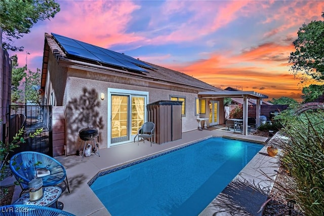 rear view of property featuring stucco siding, a patio, roof mounted solar panels, fence, and a fenced in pool