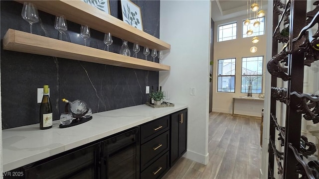 bar featuring light wood-type flooring, backsplash, light stone counters, and decorative light fixtures