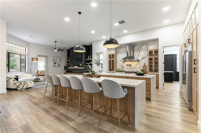 kitchen with pendant lighting, wall chimney exhaust hood, a large island, and light wood-type flooring