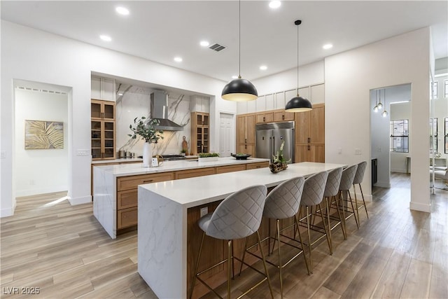 kitchen with a large island, built in refrigerator, hanging light fixtures, a kitchen bar, and wall chimney exhaust hood