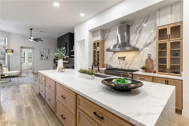 kitchen with sink, tasteful backsplash, a center island with sink, wall chimney exhaust hood, and light wood-type flooring