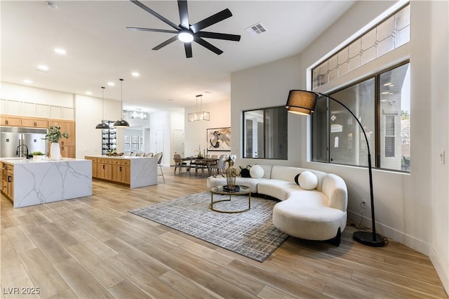 living room featuring ceiling fan, sink, and light wood-type flooring