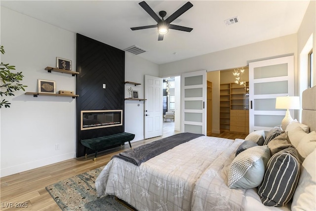 bedroom with ceiling fan with notable chandelier, a large fireplace, and light hardwood / wood-style floors