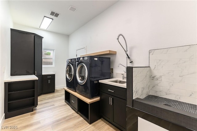 clothes washing area featuring sink, light hardwood / wood-style floors, cabinets, and washing machine and clothes dryer