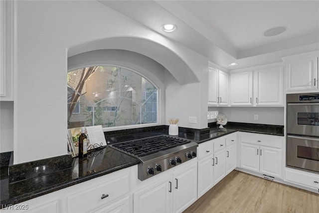 kitchen featuring white cabinetry, stainless steel appliances, light hardwood / wood-style floors, and dark stone countertops