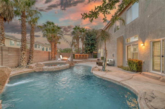 pool at dusk with a patio area, pool water feature, and an in ground hot tub