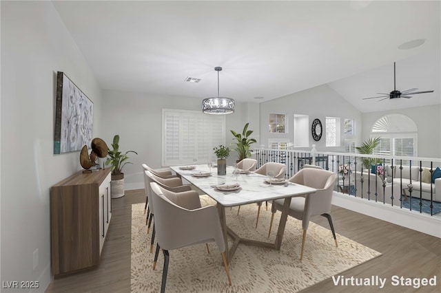 dining area featuring ceiling fan with notable chandelier, wood-type flooring, and vaulted ceiling