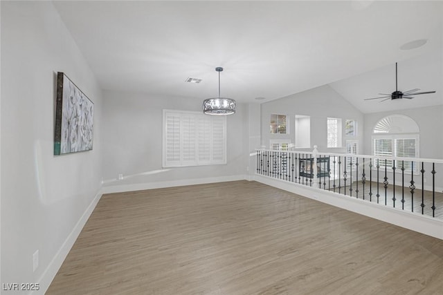 spare room featuring lofted ceiling, ceiling fan with notable chandelier, and wood-type flooring