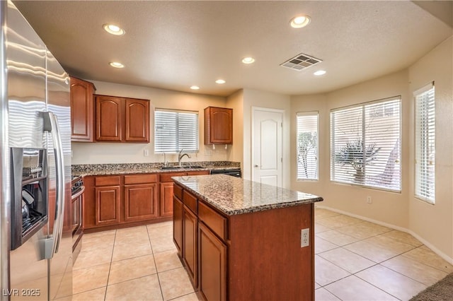 kitchen with light tile patterned flooring, sink, light stone counters, appliances with stainless steel finishes, and a kitchen island