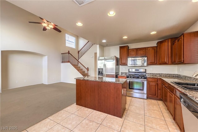 kitchen with sink, appliances with stainless steel finishes, light stone countertops, a kitchen island, and light carpet