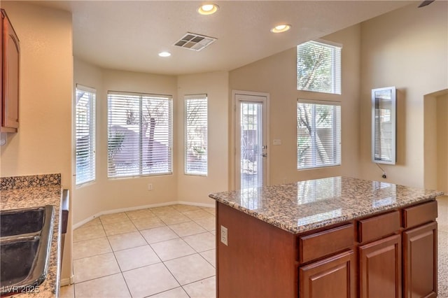 kitchen featuring light tile patterned flooring, a center island, sink, and light stone counters