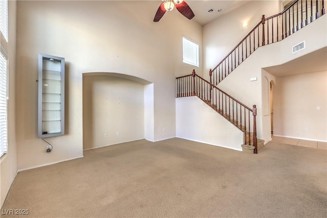 unfurnished living room featuring carpet, a towering ceiling, and ceiling fan