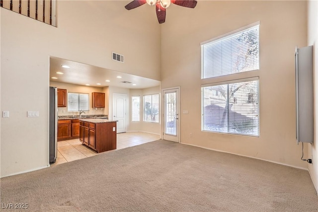 kitchen with sink, a center island, light carpet, stainless steel refrigerator, and a towering ceiling