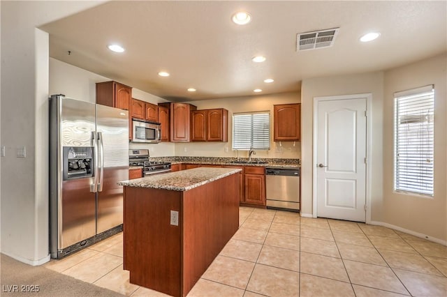 kitchen with light tile patterned floors, a kitchen island, sink, and appliances with stainless steel finishes