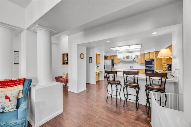 kitchen featuring a kitchen breakfast bar, black appliances, dark hardwood / wood-style flooring, kitchen peninsula, and ornate columns