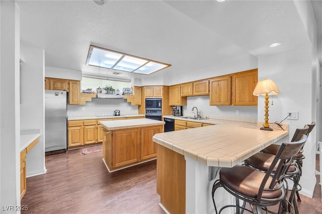 kitchen featuring a breakfast bar area, dark hardwood / wood-style floors, kitchen peninsula, a kitchen island, and black appliances