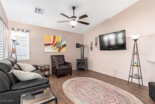 living room featuring ceiling fan, vaulted ceiling, and a wood stove