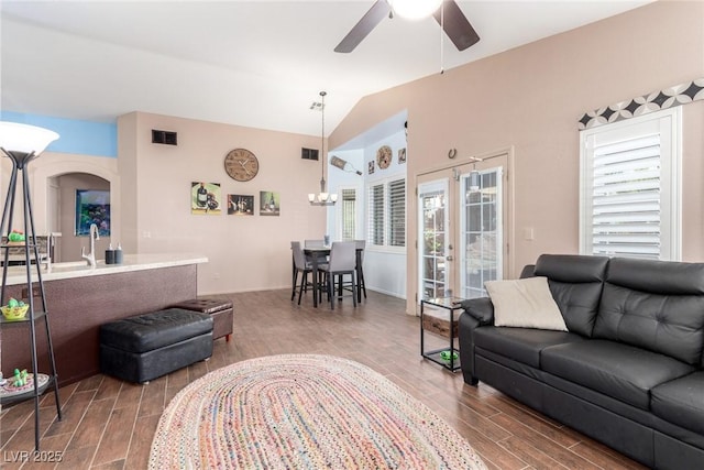 living room with a wealth of natural light, vaulted ceiling, french doors, and ceiling fan with notable chandelier