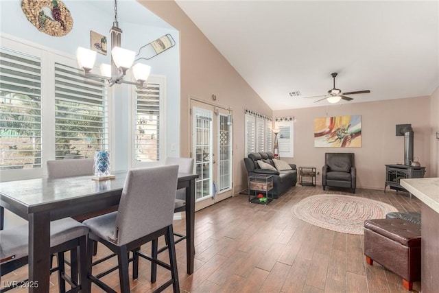 dining space featuring french doors, vaulted ceiling, a wood stove, hardwood / wood-style flooring, and ceiling fan with notable chandelier