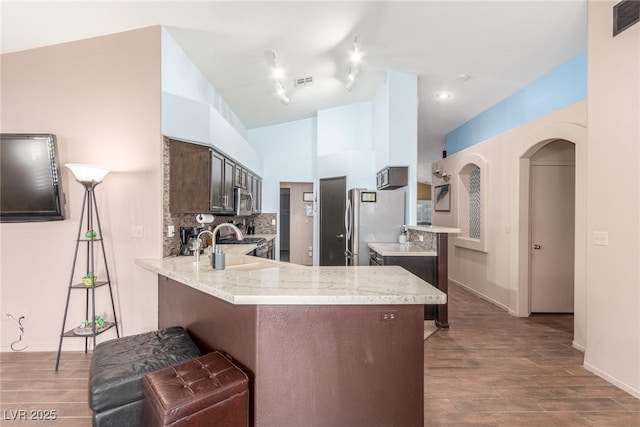 kitchen with dark brown cabinetry, light wood-type flooring, kitchen peninsula, stainless steel appliances, and backsplash