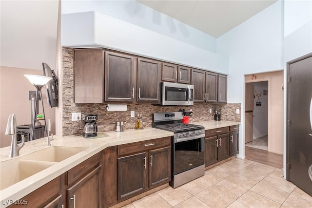 kitchen featuring light tile patterned flooring, sink, dark brown cabinets, appliances with stainless steel finishes, and backsplash