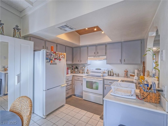 kitchen with gray cabinets, light tile patterned flooring, washer / dryer, a tray ceiling, and white appliances