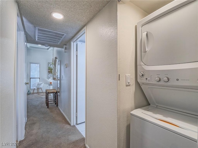 laundry room with stacked washer / drying machine, light colored carpet, and a textured ceiling