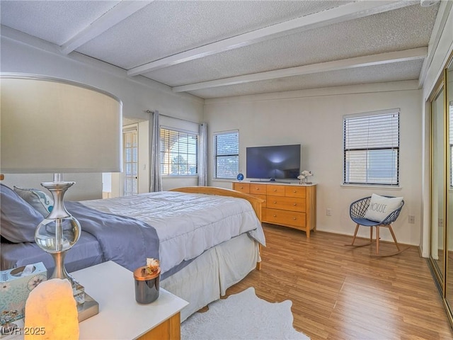 bedroom with beam ceiling, light hardwood / wood-style floors, and a textured ceiling