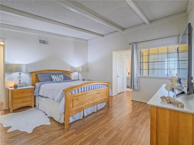 bedroom featuring beam ceiling, light hardwood / wood-style floors, and a textured ceiling