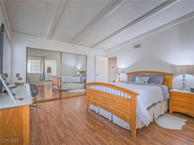 bedroom with beam ceiling, a closet, a textured ceiling, and light hardwood / wood-style flooring