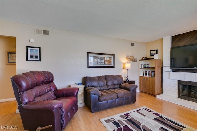 living room featuring a textured ceiling, a brick fireplace, and light hardwood / wood-style flooring