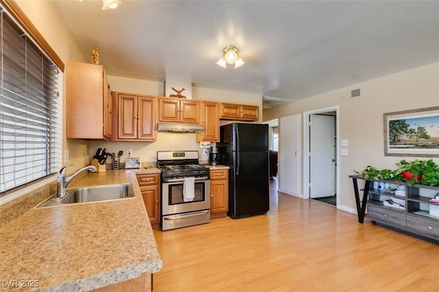 kitchen featuring stainless steel range with gas cooktop, black refrigerator, sink, and light wood-type flooring