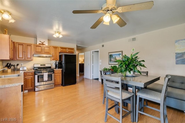 kitchen with stainless steel range with gas cooktop, sink, ceiling fan, black fridge, and light hardwood / wood-style flooring