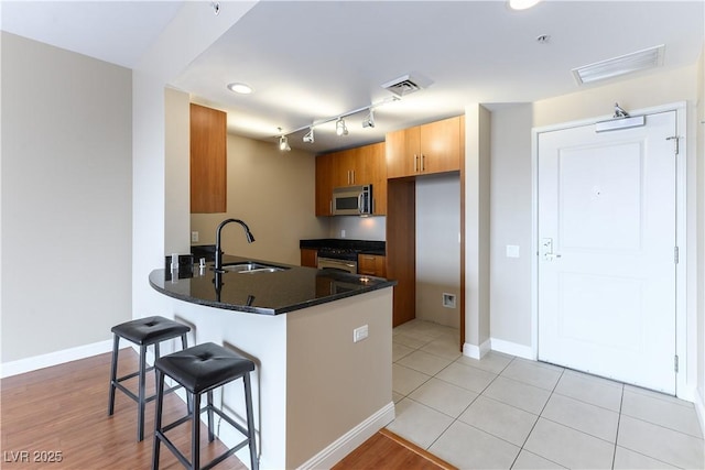 kitchen featuring sink, light tile patterned floors, appliances with stainless steel finishes, a kitchen breakfast bar, and kitchen peninsula