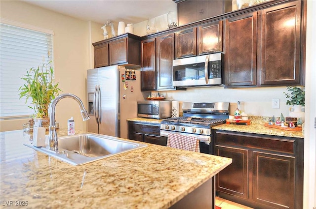 kitchen with dark brown cabinetry, sink, light stone counters, and stainless steel appliances