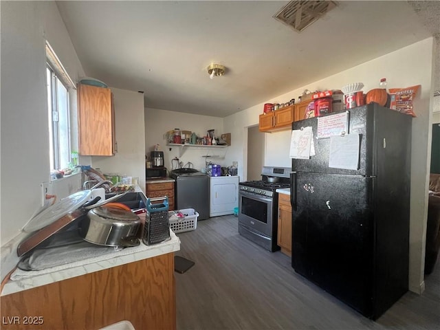 1900 W Carey Ave, North Las Vegas, NV 89032 - kitchen with black refrigerator, dark hardwood / wood-style floors, washer and dryer, tile countertops, and stainless steel range with gas cooktop