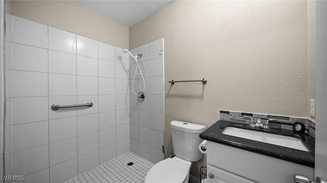 bathroom with a textured wall, a tile shower, vanity, and toilet