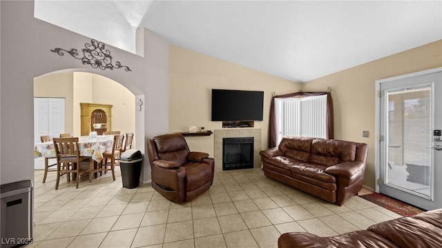 living area featuring lofted ceiling, light tile patterned floors, a tile fireplace, and arched walkways