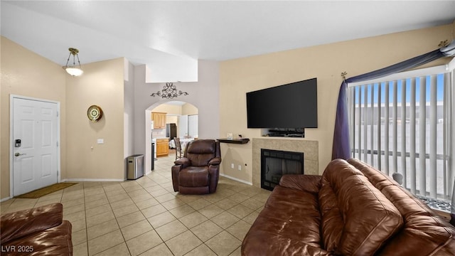 living area with arched walkways, light tile patterned floors, a tiled fireplace, vaulted ceiling, and baseboards