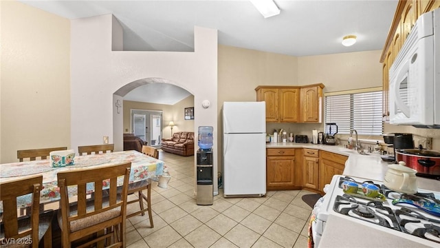 kitchen featuring white appliances, arched walkways, light countertops, a sink, and light tile patterned flooring