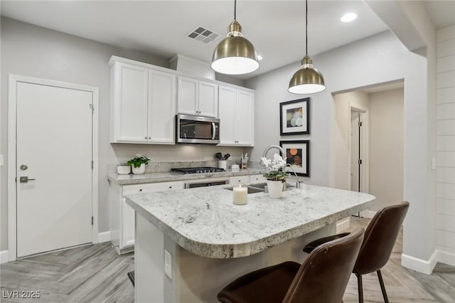 kitchen featuring a center island with sink, visible vents, white cabinets, appliances with stainless steel finishes, and a kitchen bar