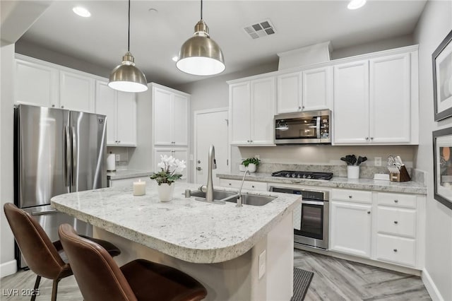 kitchen featuring a center island with sink, visible vents, a sink, stainless steel appliances, and white cabinetry