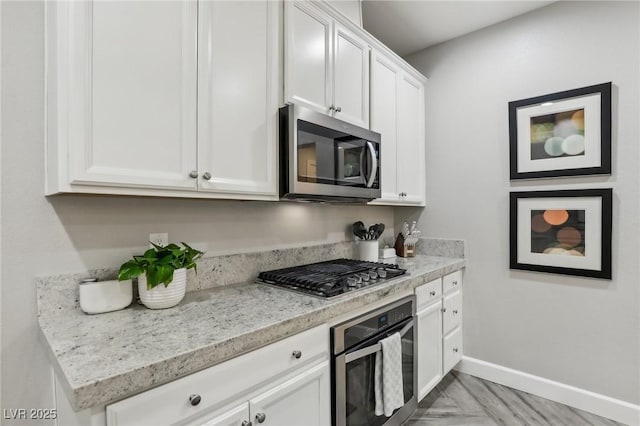 kitchen featuring light stone counters, white cabinetry, stainless steel appliances, and baseboards