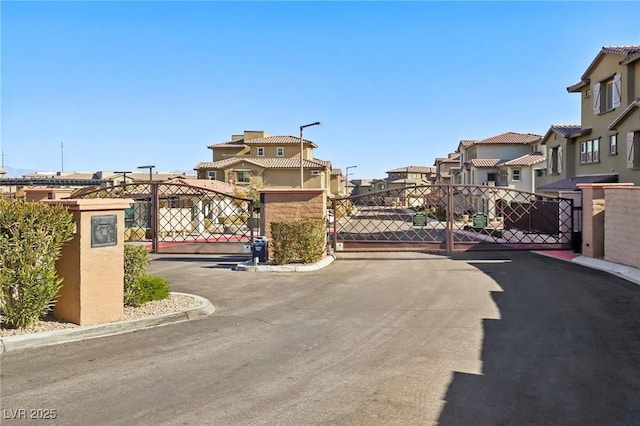 view of road featuring a gate, curbs, a residential view, and a gated entry