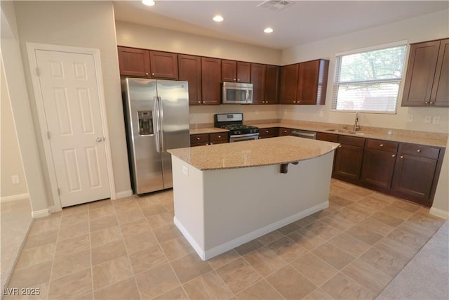 kitchen with sink, appliances with stainless steel finishes, dark brown cabinets, a center island, and light stone counters