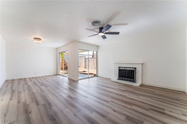 unfurnished living room with ceiling fan, a fireplace, light hardwood / wood-style flooring, and a textured ceiling