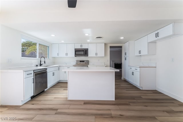 kitchen with sink, a kitchen island, stainless steel appliances, light hardwood / wood-style floors, and white cabinets