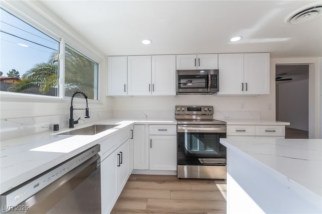 kitchen with sink, white cabinetry, light stone counters, stainless steel appliances, and light hardwood / wood-style floors