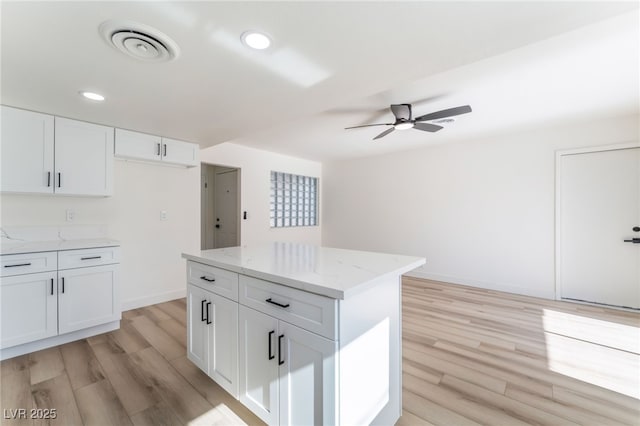 kitchen featuring light stone counters, a center island, light wood-type flooring, and white cabinets