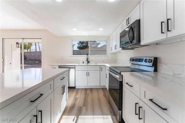 kitchen with sink, stainless steel appliances, light stone counters, light hardwood / wood-style floors, and white cabinets